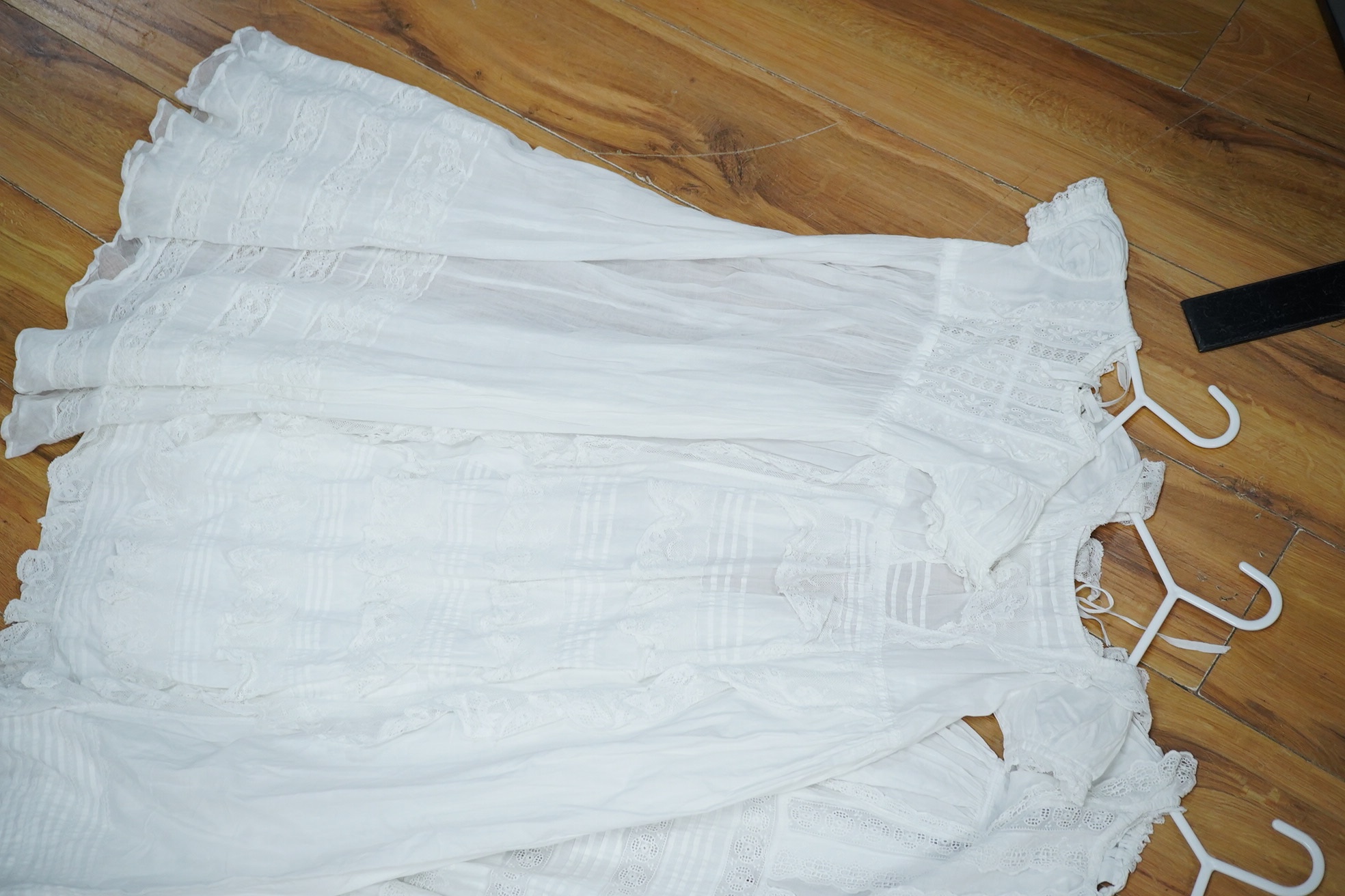 An Edwardian cream silk christening gown, together with four white christening gowns and a baby gown. The silk christening gown edged and inserted with lace and feather stitch embroidery, one Christening gown worked with